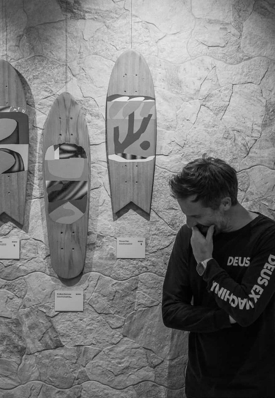 Mat Macready standing next to wall-mounted skateboards he created for Currents Solo Show.